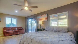 A bedroom with a large bed, a ceiling fan, a window with blinds, a brown leather couch, and a painting on the wall. - Luxury Estate - Sleep 24 - Infinity Pool & Hot Tub (Vista)