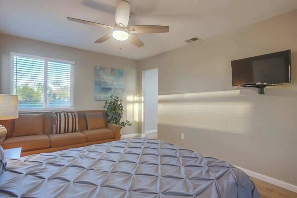 A bedroom with a bed, a ceiling fan, a TV mounted on the wall, a window with blinds, and a couch. - Luxury Estate - Sleep 24 - Infinity Pool & Hot Tub (Vista)