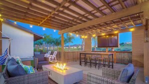 An outdoor patio with wicker furniture, a fire pit, and a TV screen. - Luxury Estate - Sleep 24 - Infinity Pool & Hot Tub (Vista)