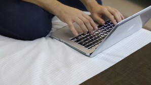 A person sitting on a bed using a laptop. - Margarett Hotel (Valladolid)
