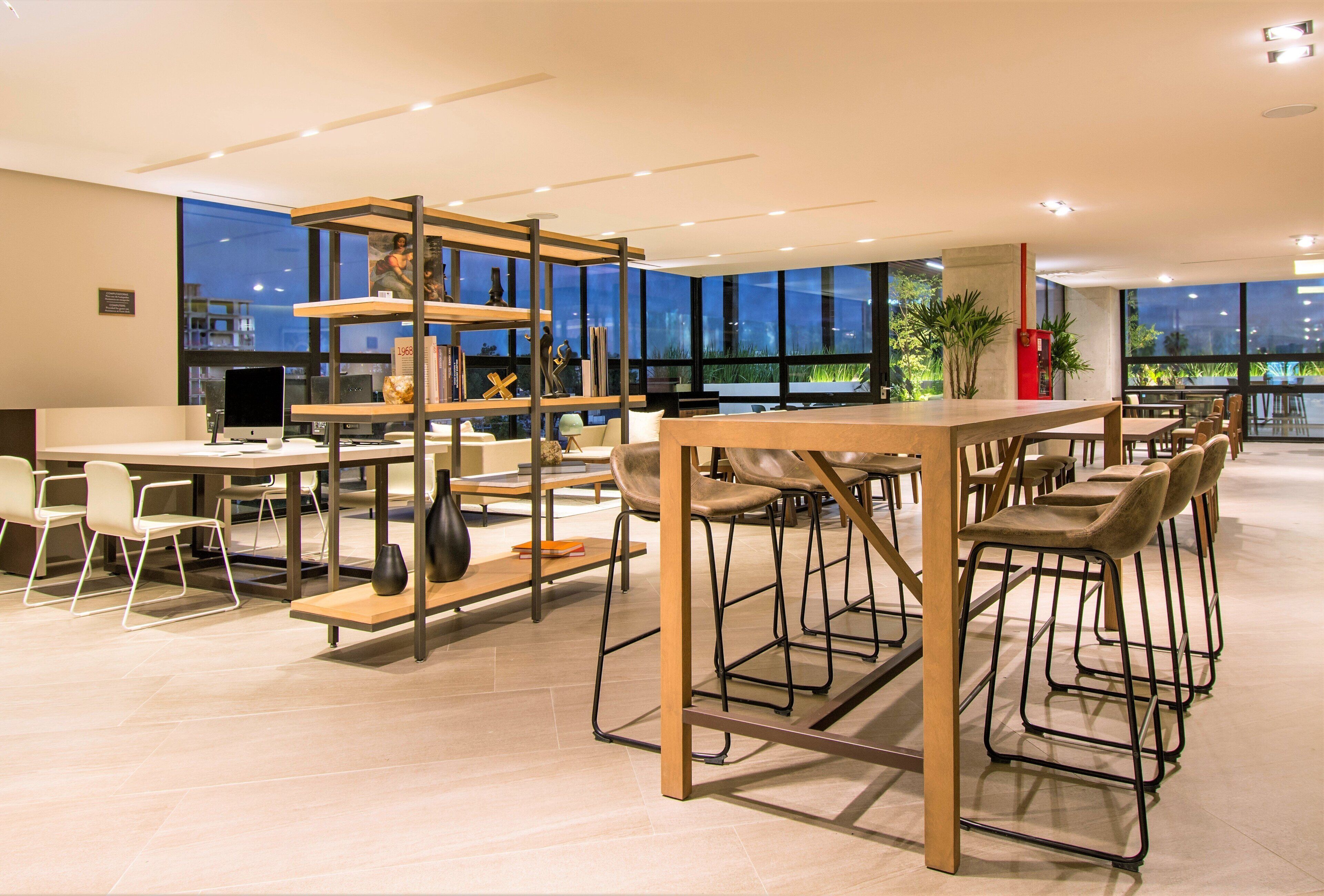 A modern office space with a long table, bar stools, and a bookshelf.