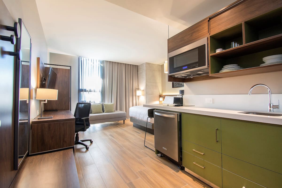 Een moderne hotelkamer met een kitchenette, een bank, een bureau en uitzicht op de stad.
