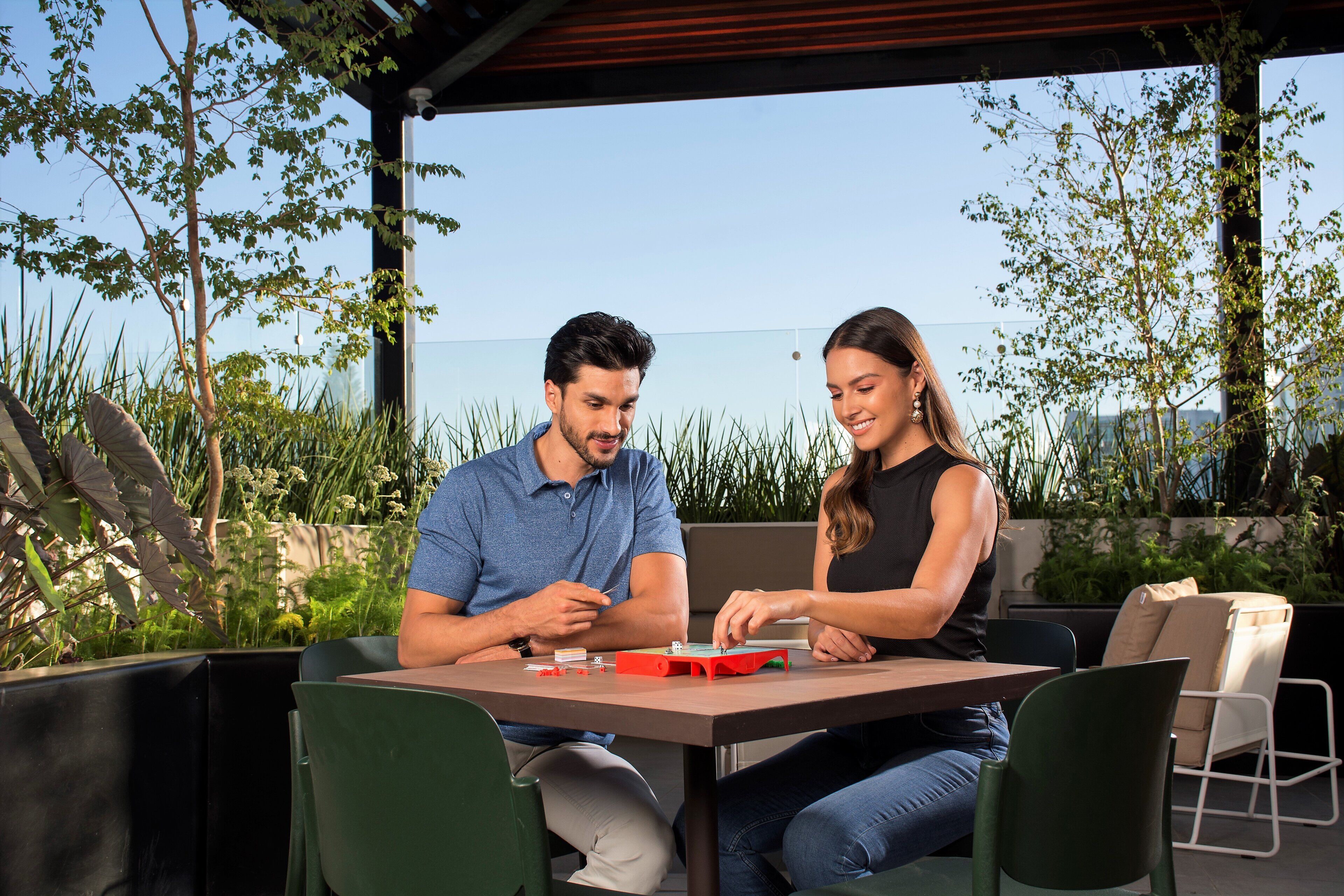 Dos personas sentadas en una mesa al aire libre con vista al mar, rodeadas de vegetación.