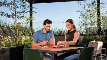 Dos personas sentadas en una mesa al aire libre con vista al mar, rodeadas de vegetación.