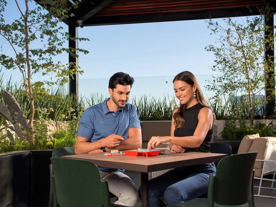 Zwei Personen sitzen an einem Tisch im Freien mit Blick auf das Meer, umgeben von viel Grün.