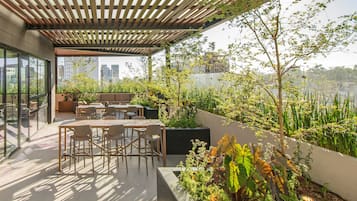 A rooftop terrace with a wooden pergola, outdoor seating, and lush greenery.