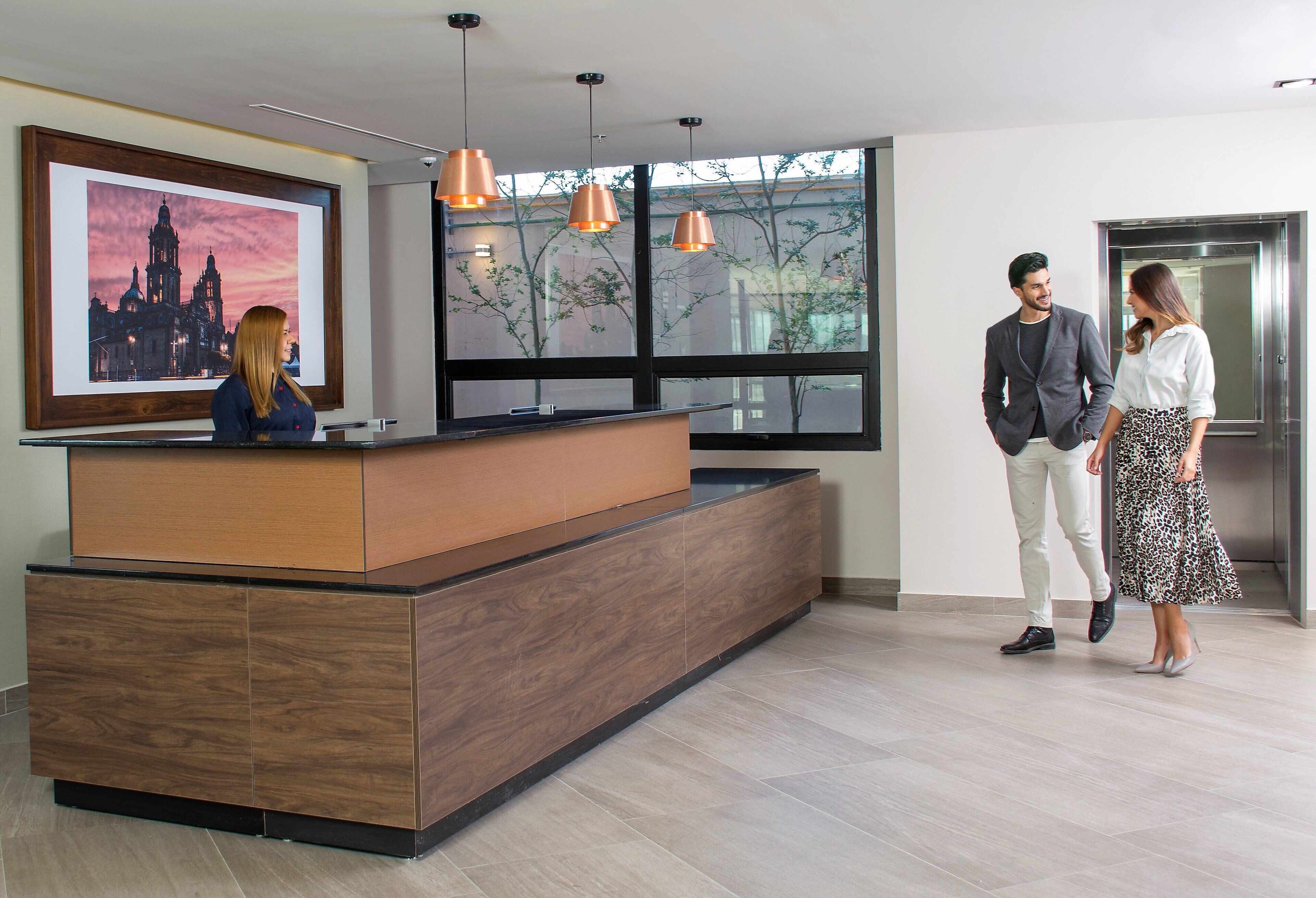 A reception desk with a large framed cityscape picture, a modern wooden counter, and pendant lighting.