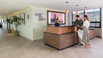 A reception area with a wooden reception desk, framed artwork on the wall, and potted plants.