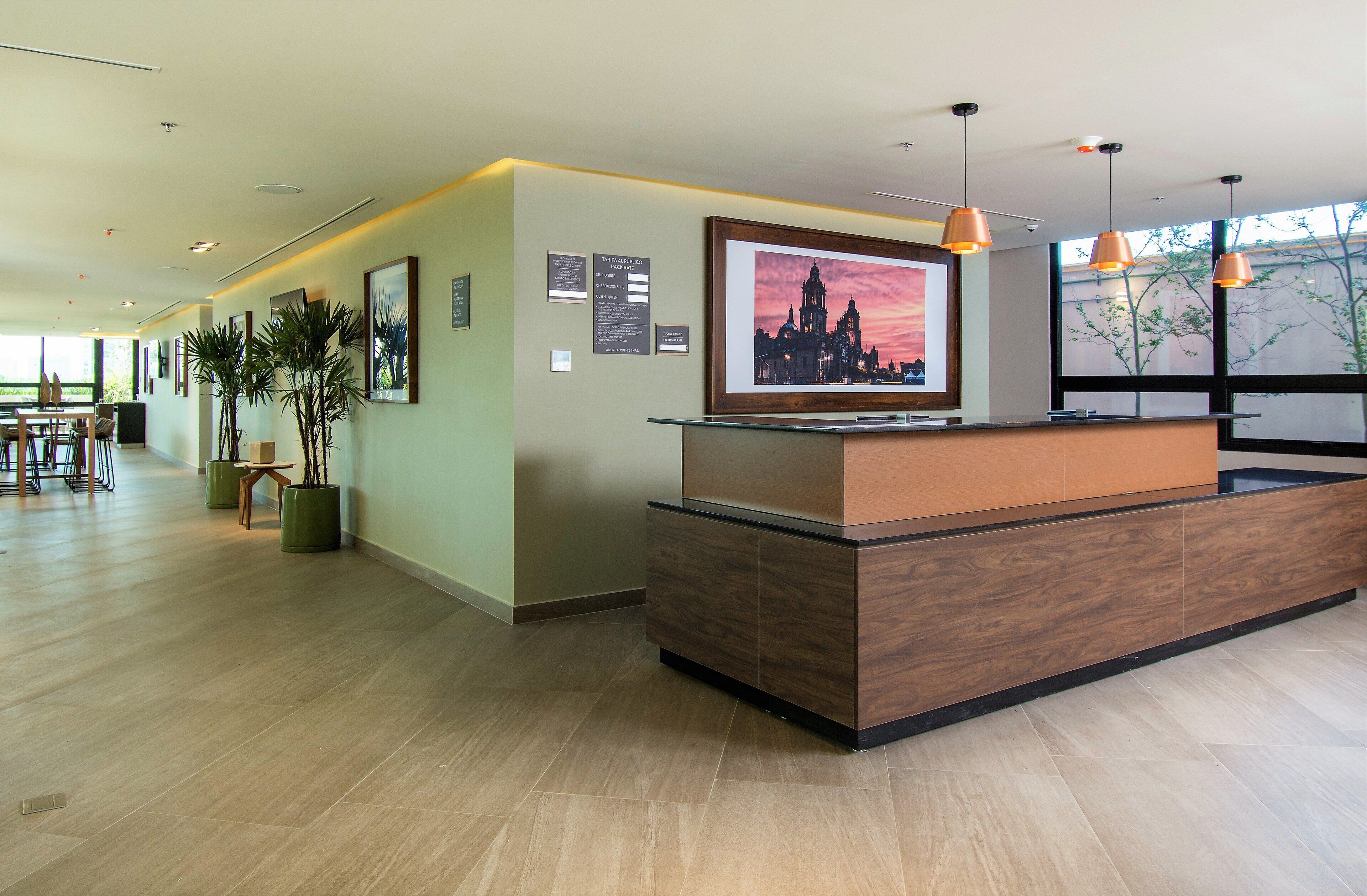 A reception area with a wooden reception desk, framed artwork on the wall, and potted plants.