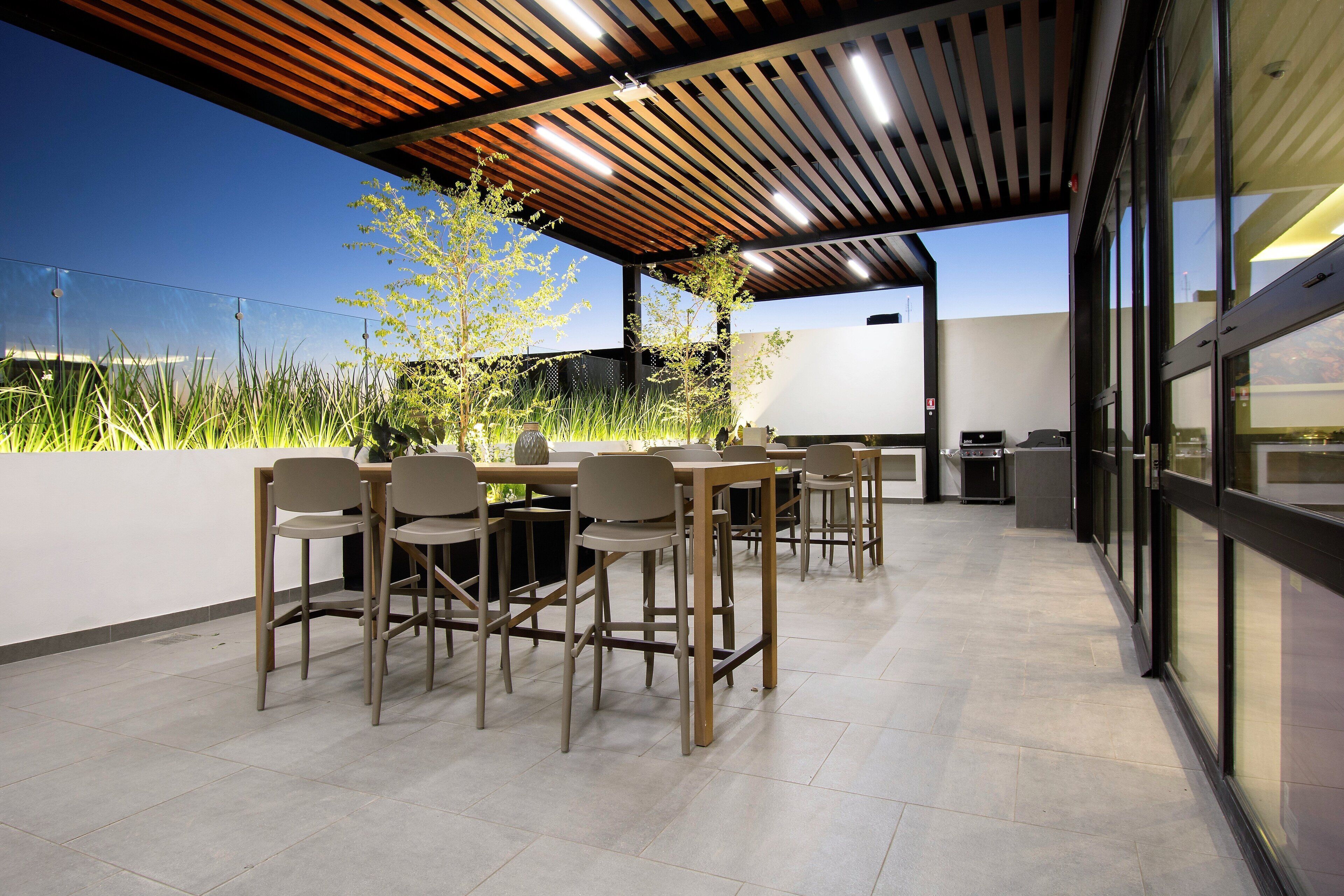 Ein Essbereich im Freien mit Holztischen und -stühlen, einer Pergola darüber und Blick zum Himmel.