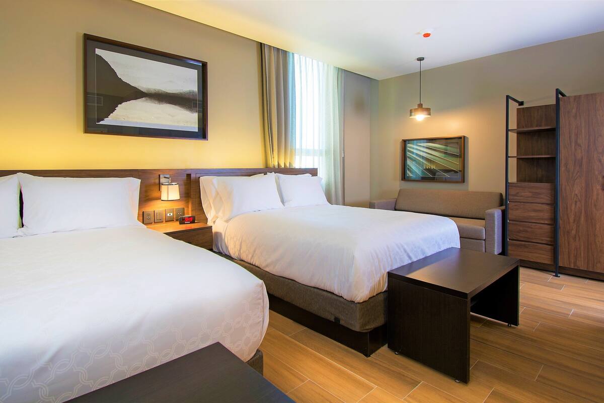 Een hotelkamer met twee bedden, een bureau, een bank, een kledingkast en een schilderij aan de muur.