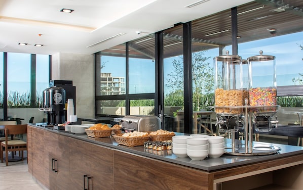 Um balcão de café da manhã moderno com máquina de café, cestos de pão e distribuidores de cereais.