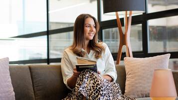Eine Person sitzt auf einem Sofa mit einem Buch in einem Zimmer mit einer modernen Lampe und einem großen Fenster.
