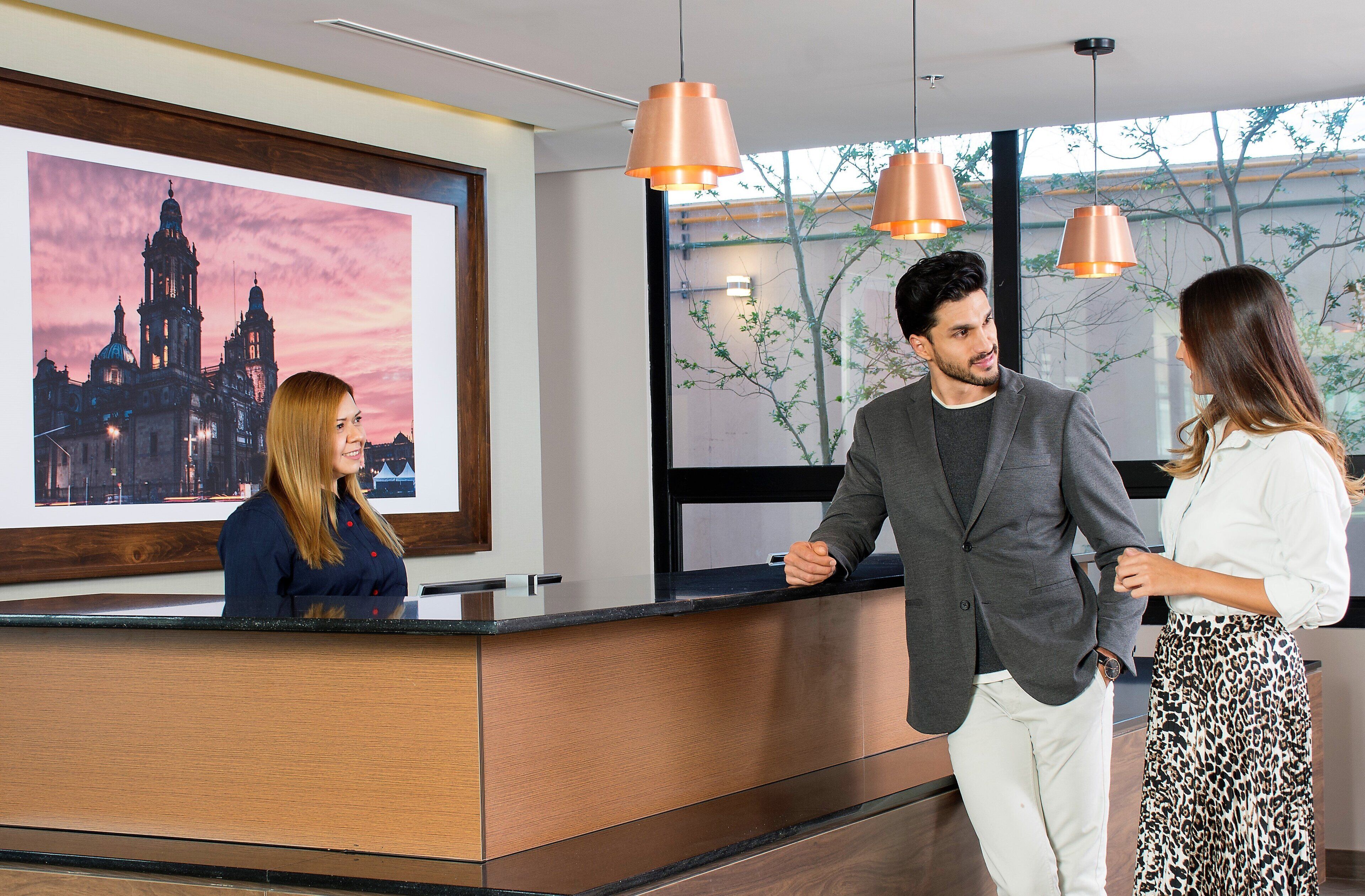 A reception desk with a framed picture of a cathedral, a modern interior with pendant lighting, and a view of trees through the window.
