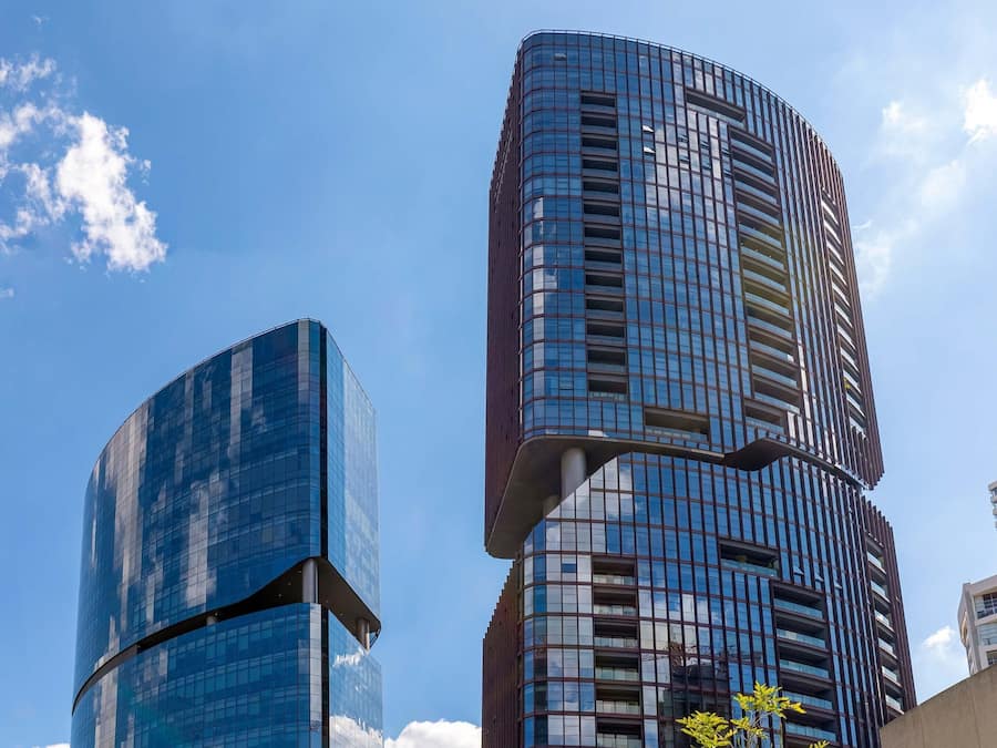 Un moderno edificio de gran altura con fachada de vidrio curva, varios balcones y un cielo azul despejado al fondo.