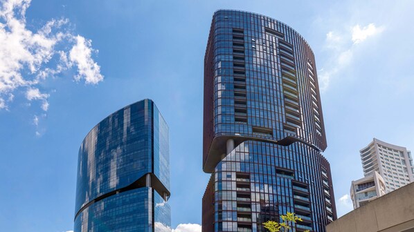 Un moderno edificio de gran altura con fachada de vidrio curva, varios balcones y un cielo azul despejado al fondo.