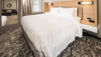 Une chambre d’hôtel dotée d’un grand lit, d’une table de chevet avec une horloge numérique, d’une tête de lit avec éclairage intégré et d’une moquette à motifs.