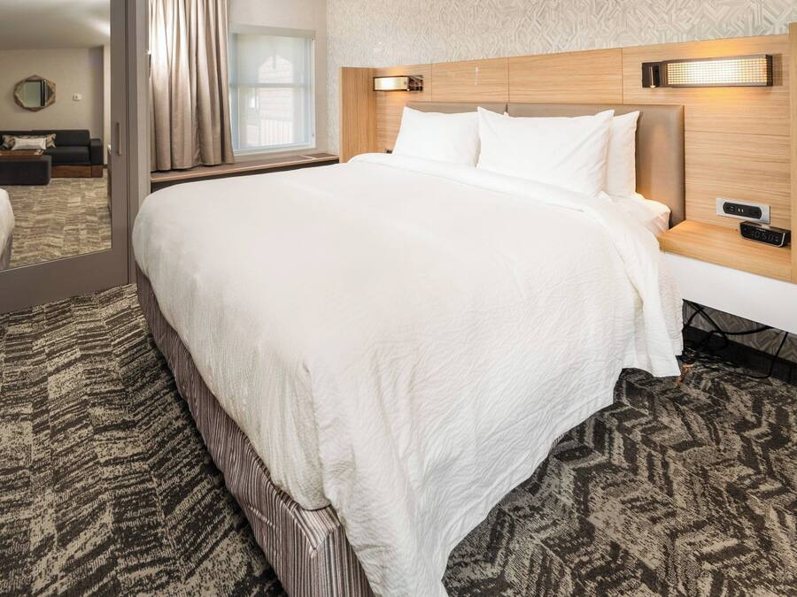 Une chambre d’hôtel dotée d’un grand lit, d’une table de chevet avec une horloge numérique, d’une tête de lit avec éclairage intégré et d’une moquette à motifs.