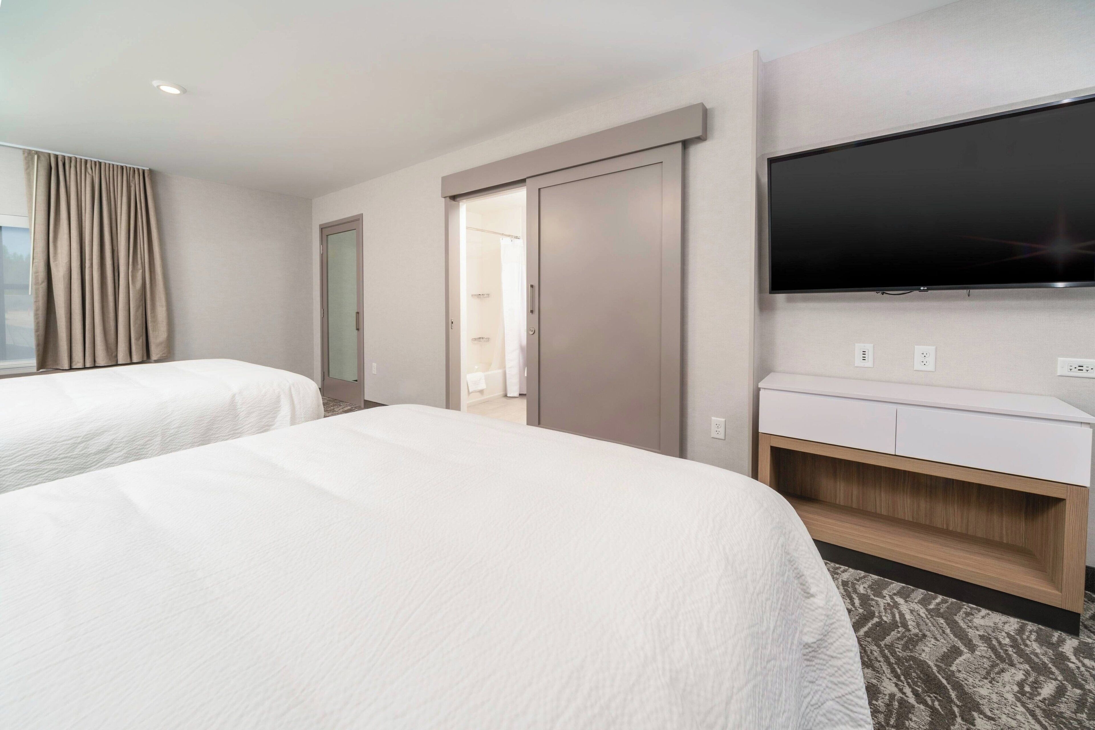 A hotel room with two beds, a TV mounted on the wall, and a sliding door leading to a bathroom.
