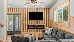 A modern living room with a large sectional sofa, a fireplace, and a flat-screen TV mounted on a wooden wall. - SpringHill Suites by Marriott Island Park Yellowstone (Island Park)