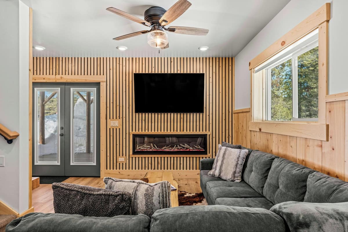 Een moderne woonkamer met een grote hoekbank, een open haard en een flatscreen televisie bevestigd aan een houten wand.