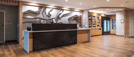 A modern reception area with a wooden reception desk, a wall-mounted display, and a bookshelf filled with magazines.
