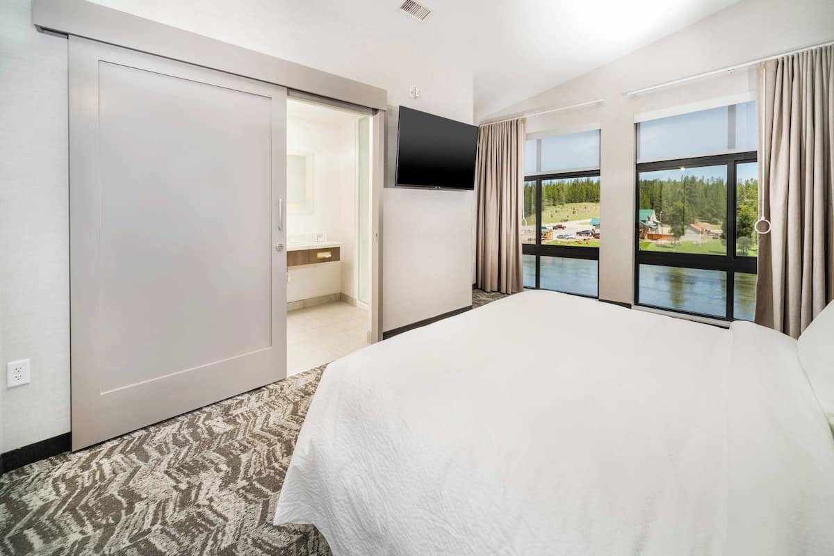 Une chambre d’hôtel dotée d’un grand lit, d’un placard avec porte coulissante, d’un téléviseur à écran plat et d’une fenêtre donnant sur un lac et des bâtiments.