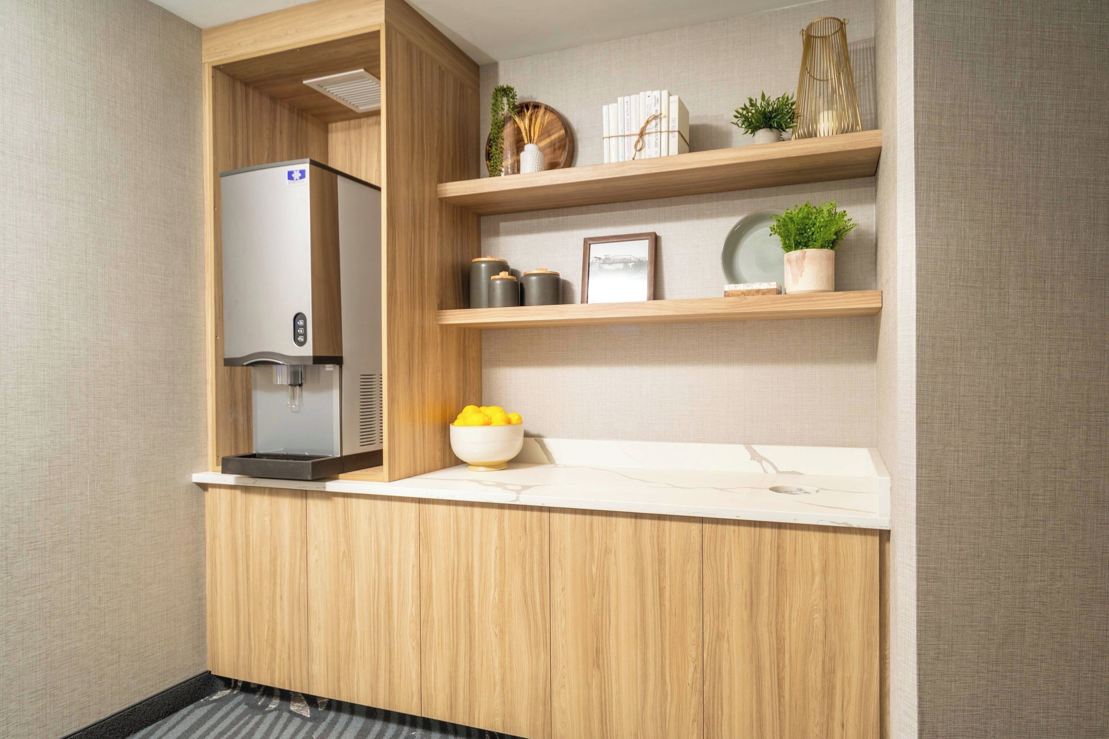 A compact kitchenette with a built-in refrigerator, a sink, and wooden shelves with decorative items.