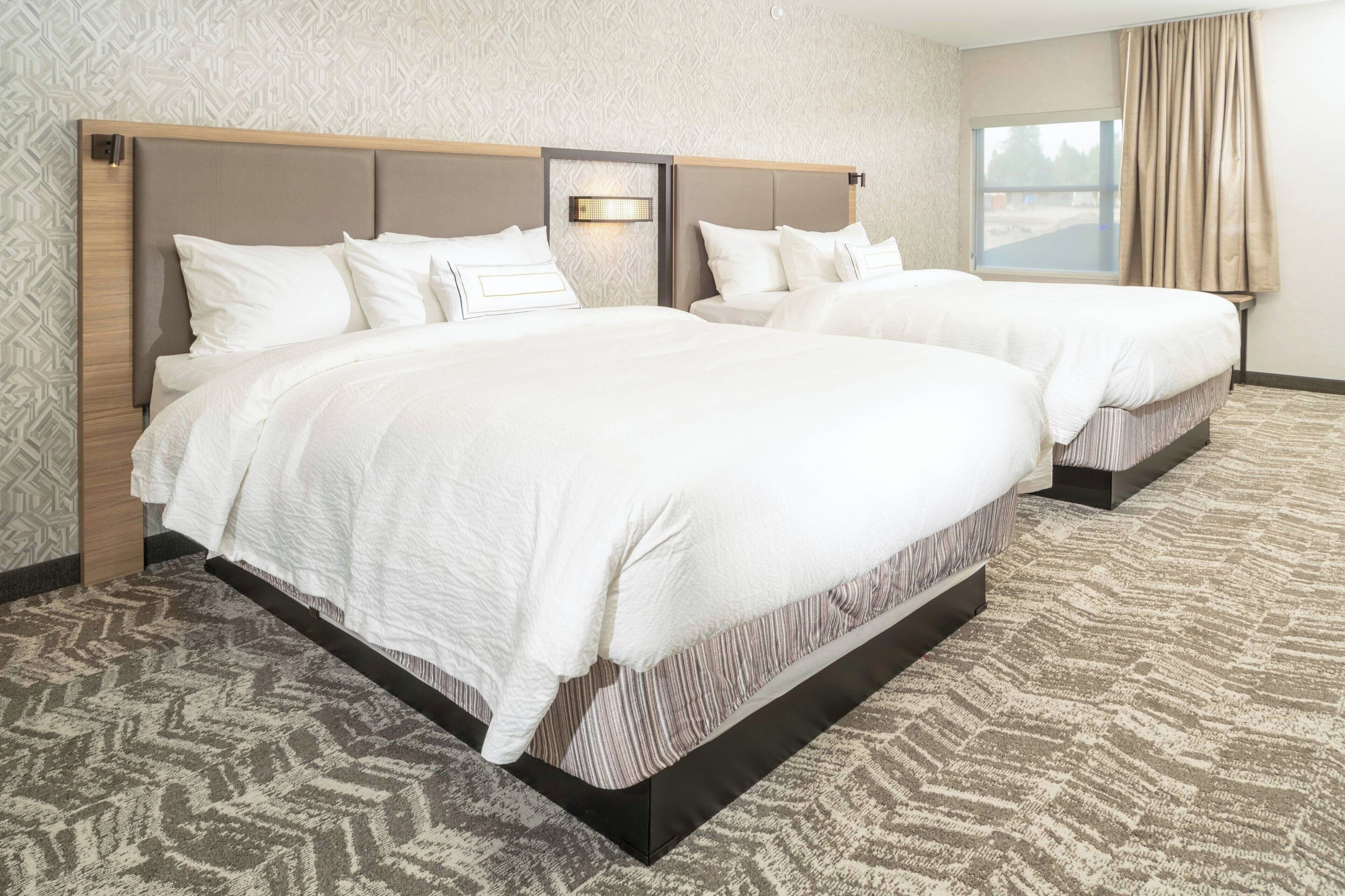 A hotel room with two beds, a patterned carpet, and a window with curtains.