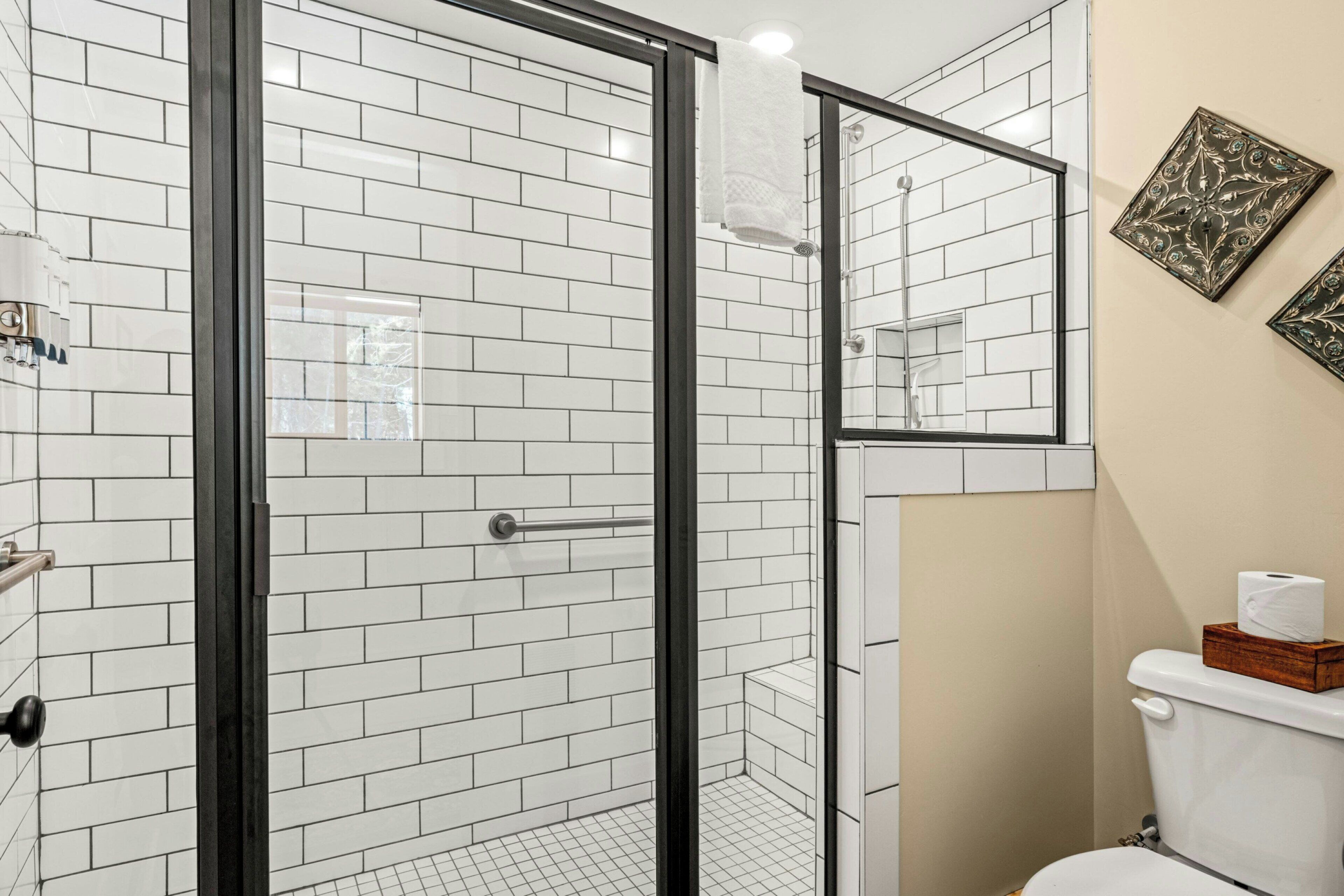 A bathroom with white subway tiles, a glass-enclosed shower, a toilet with a wooden box, and a mirror.