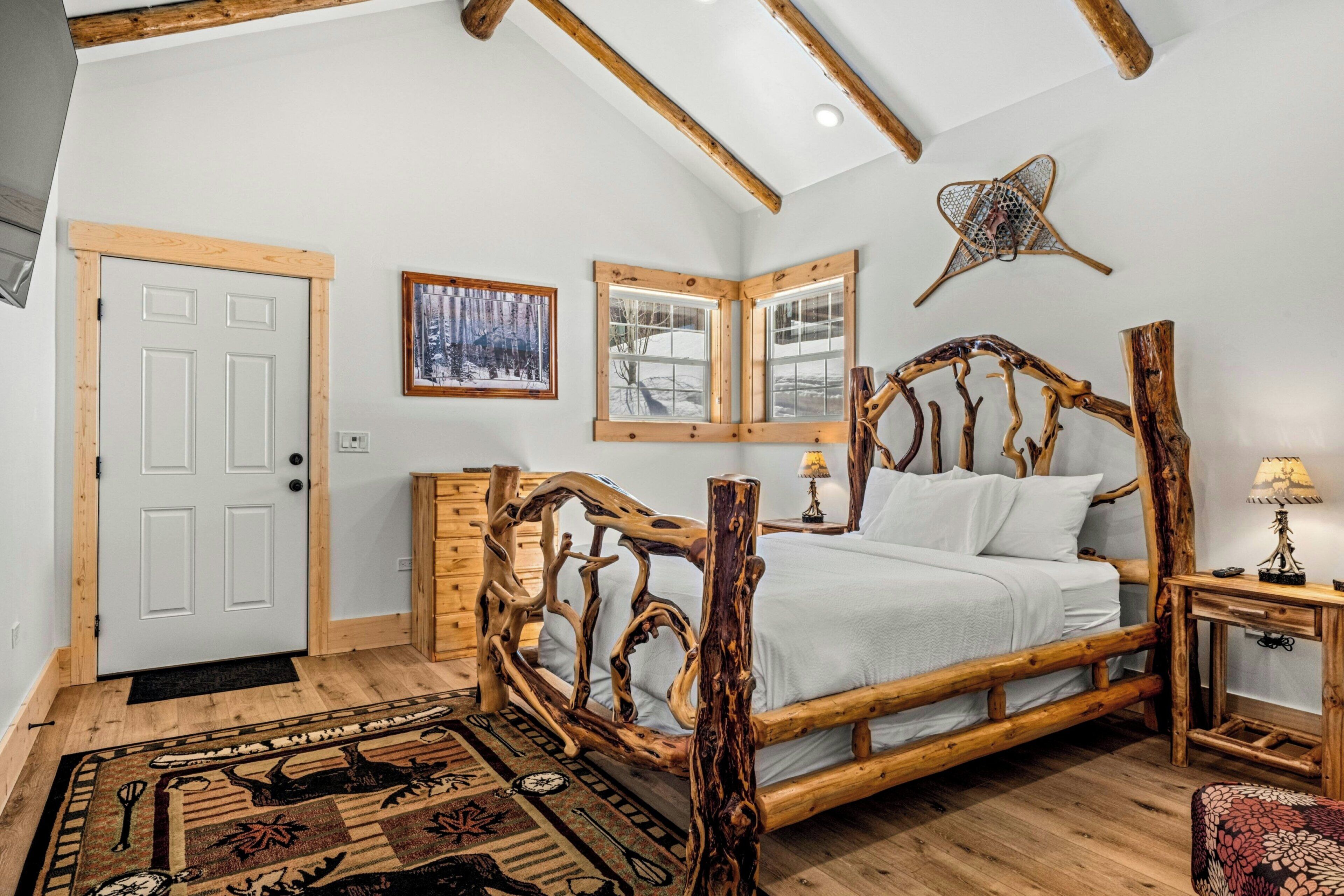 A bedroom with a wooden bed frame, a window with a view, and a door.