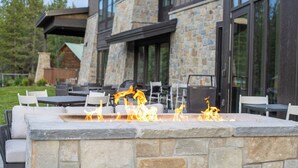 An outdoor patio with stone fire feature, outdoor seating, and a stone building in the background. - SpringHill Suites by Marriott Island Park Yellowstone (Island Park)