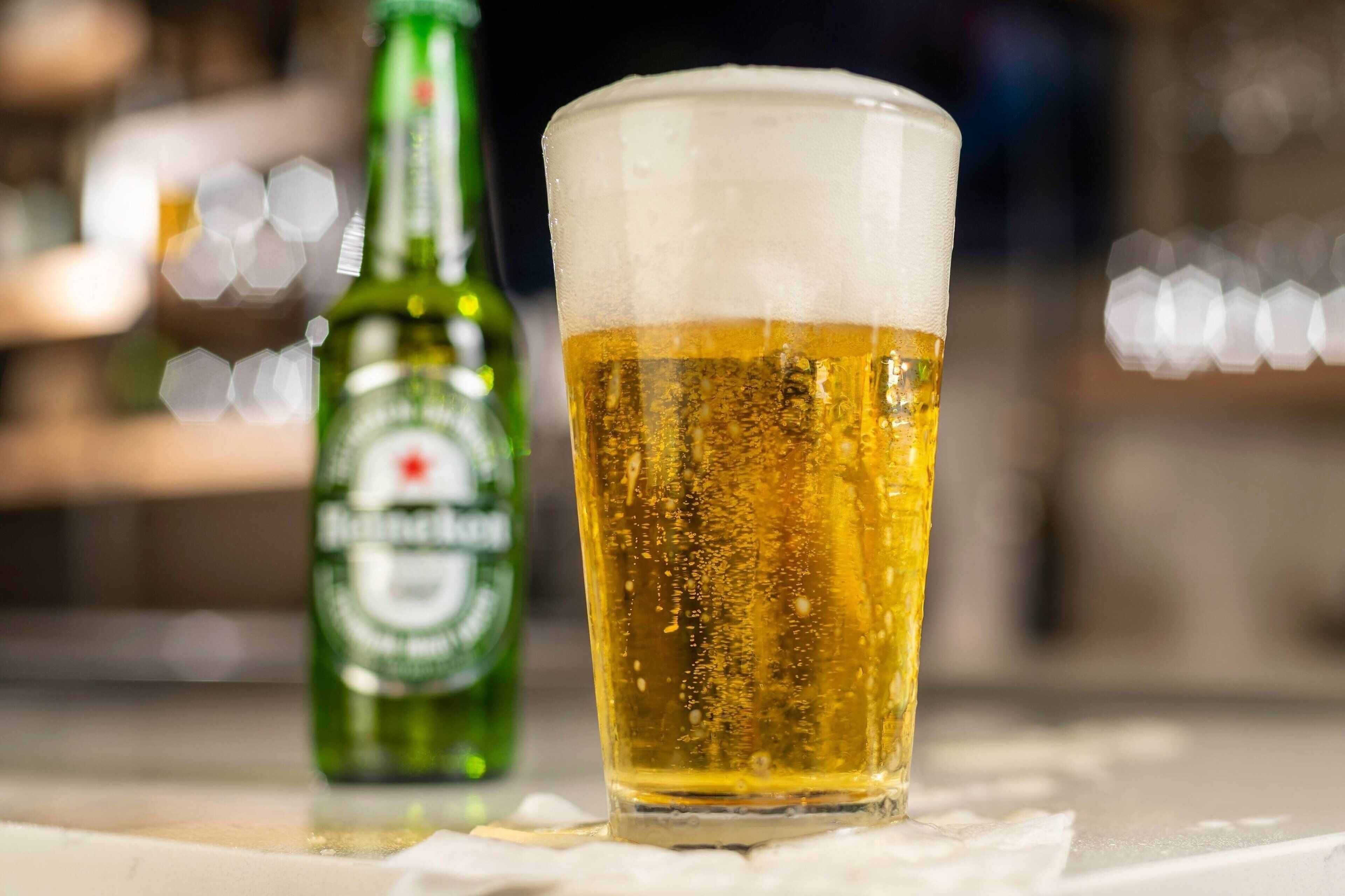 Un verre de bière avec une mousse généreuse, posé sur le comptoir d’un bar, avec une bouteille de bière en arrière-plan.