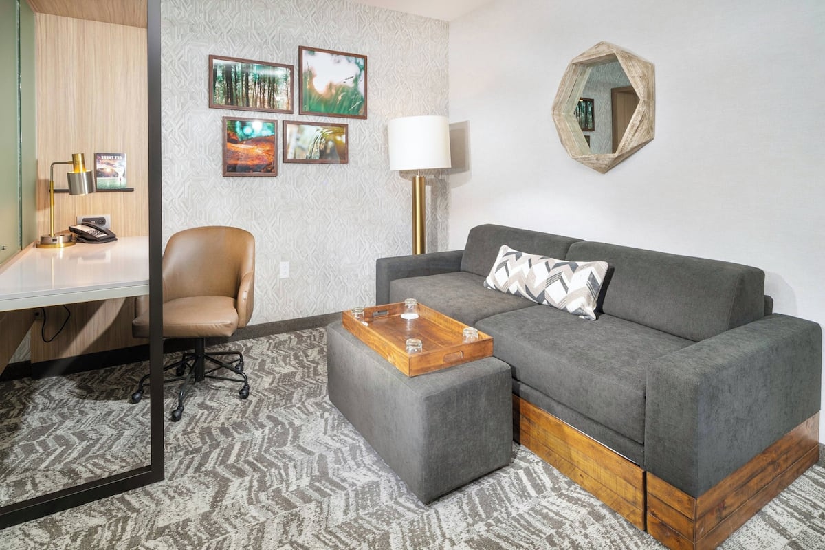 Un salon moderne avec un canapé gris, une table basse en bois, un fauteuil gris, un bureau avec une lampe et des tableaux encadrés accrochés au mur.