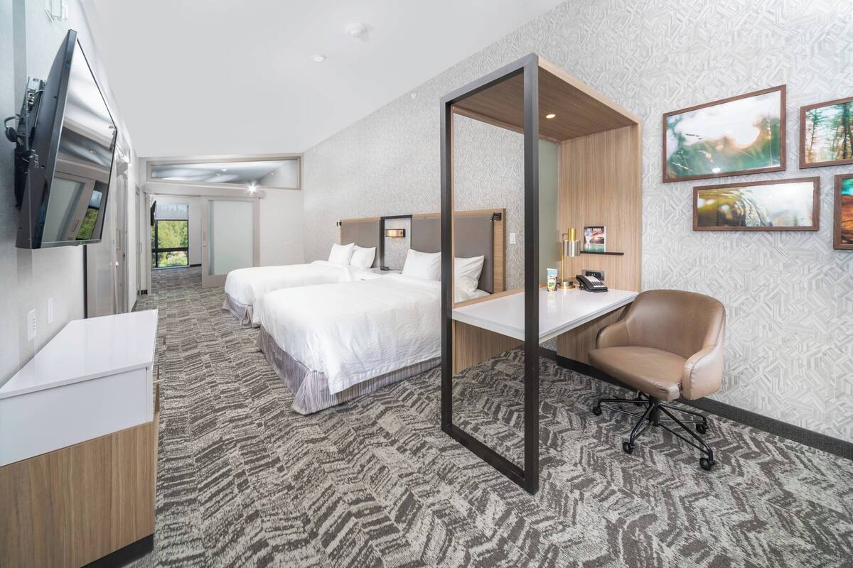 Een hotelkamer met twee bedden, een bureau, een stoel, een televisie en kunst aan de muur.