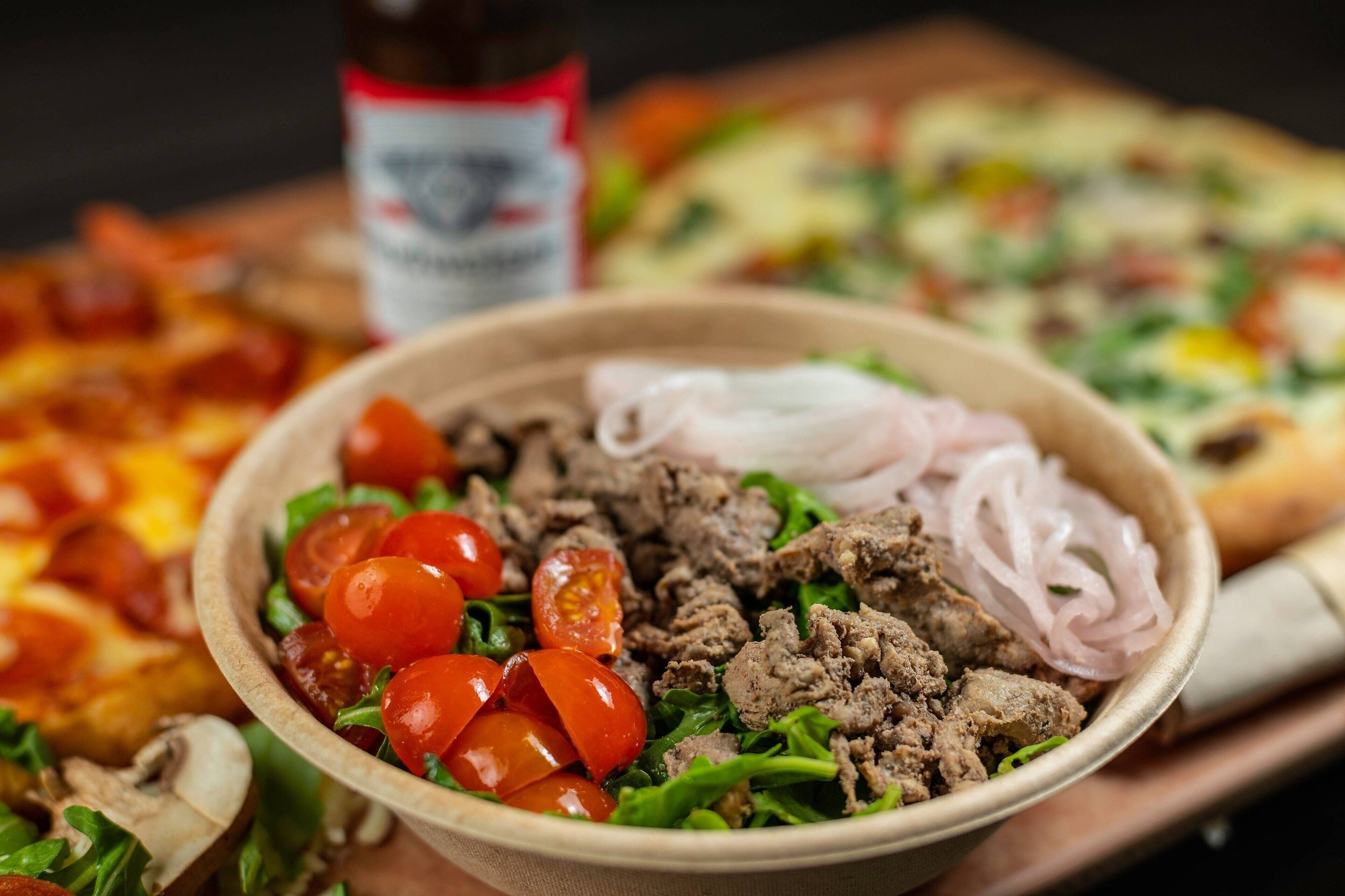 A bowl of salad with meat, tomatoes, and onions.