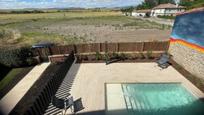 Una piscina amb terrassa de fusta, gandules i vistes a un paisatge rural.