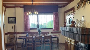 Una zona de menjador amb una taula i cadires de fusta, una làmpada penjant i una finestra amb cortines.