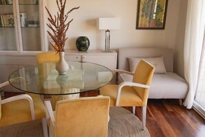 Un comedor con una mesa de vidrio, cuatro sillas, un jarrón con plantas secas, un sofá y una lámpara.
