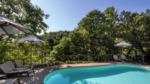 Una piscina con lettini e ombrelloni, immersa nel verde.