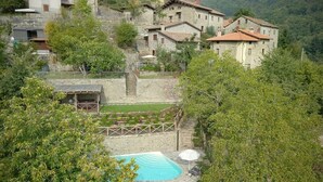 Un edificio in pietra con piscina, circondato da alberi e un giardino.