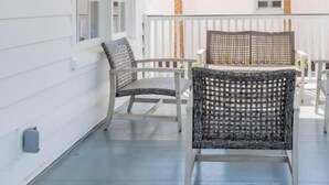 Een overdekte veranda met twee rieten stoelen, een witte balustrade en een wandlamp.