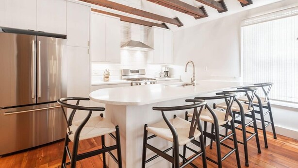 Een moderne keuken met een centraal eiland, roestvrijstalen apparatuur en zwarte barkrukken.