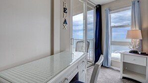 Ein Zimmer mit einem Bett, einem kleinen Tisch, einem Stuhl, einem Nachttisch und Meerblick durch ein großes Fenster.