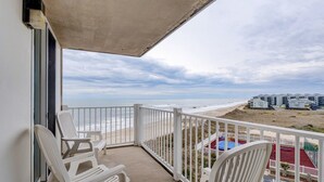 Ein Balkon mit weißen Stühlen, einem Pool und Blick auf Strand und Meer.