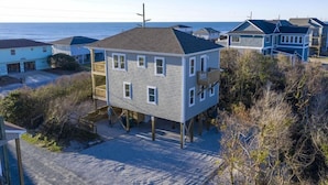 Une maison à deux étages avec un balcon, construite sur pilotis près de la plage.