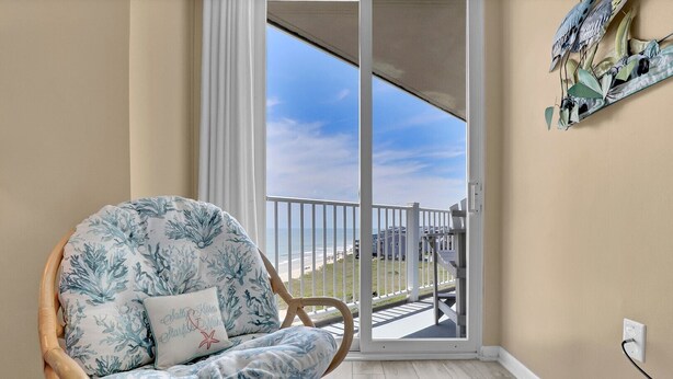 Una stanza con una sedia in vimini, vista sulla spiaggia e un balcone con ringhiera.