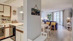 Une cuisine moderne avec des meubles blancs, un coin repas doté d’un canapé bleu et une vue sur le balcon.