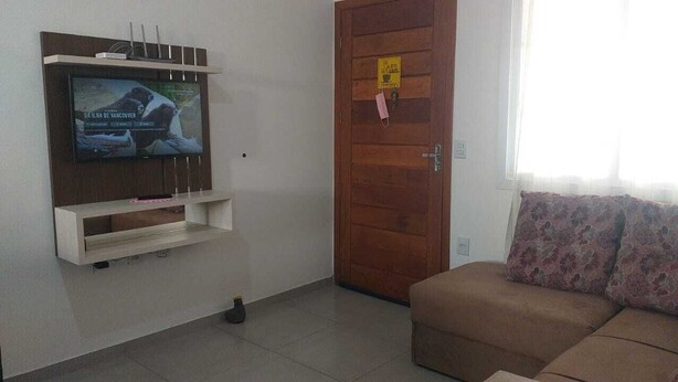 Ein Wohnzimmer mit an der Wand montiertem Fernseher, einer Holztür mit Beschilderung und einem Sofa mit floralen Kissen.
