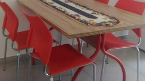 Ein rechteckiger Holztisch mit einer Tischläufer mit Blumenmuster, umgeben von sechs roten Stühlen mit Metallbeinen.